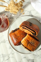 Tasty buns with poppy seeds served with tea on white marble table, flat lay