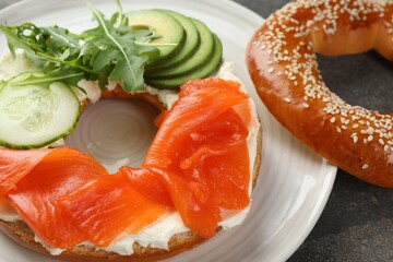 Delicious bagel with salmon, cream cheese, cucumber and avocado on grey table, closeup