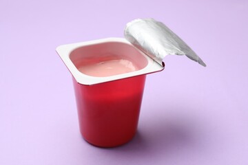Delicious yogurt in plastic cup on violet background, closeup