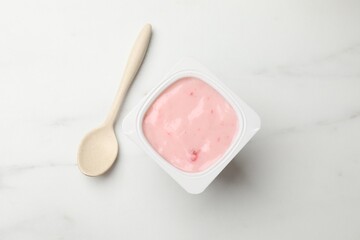 Delicious yogurt in plastic cup and spoon on light marble table, flat lay
