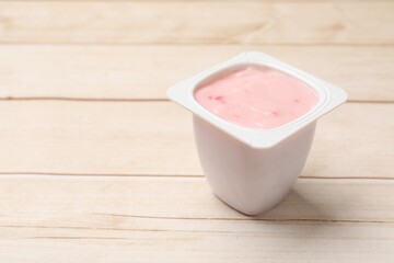 Delicious yogurt in plastic cup on wooden table, closeup. Space for text