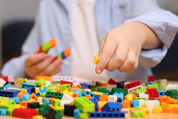 Fototapeta premium Cute boy playing with building blocks at wooden table indoors, closeup