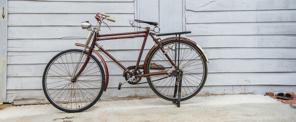 Banner panorama size of Vintage bicycle on old rustic dirty wall house, many stain on wood wall. Classic bike bicycle on decay brick wall retro style. Cement loft partition and window background.