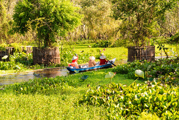 Boat with three persons on river in Asia among green tropical lanscape