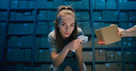Tired Female Warehouse Employee Looking at Camera, Scanning Cardboard Boxes Using Scanner. Postal Service, Logistics Center with Shelves full of Packages in Background. Blue Neon Lighting. Portrait.
