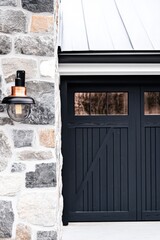 Naklejka premium The exterior scene displays a contemporary stone wall paired with sleek dark wooden garage doors, illuminated by a minimalist light fixture as dusk settles in