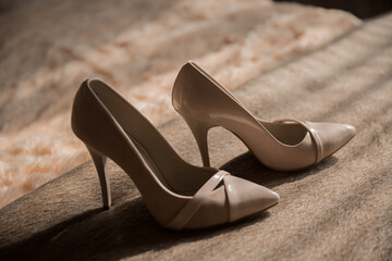 Two tan high heels are laying on a carpet. The shoes are pointed and have a high heel