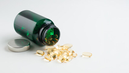 Close-up of vitamin Omega 3 or D gel capsules spilling out of green pill bottle on white table...