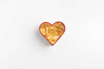 The heart made of yellow capsules of vitamin Omega 3 or D on a white background. Yellow pills of fish oil. Preventing heart disease and ischemic stroke. Skin care, depression treatment