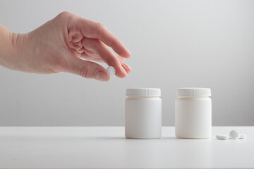 A young woman's hand holds a white pill and plastic bottles on a white background. Mockup for branding a box with pills, capsules, pills, supplements or vitamins. Healthcare concept