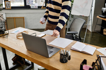 A young man in a striped sweater organizes documents at a sleek office desk during the day.