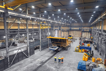 Three engineers control repair of dump car in garage of factory. Industry big yellow mining truck...