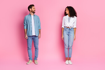 Young couple in casual outfits smiling against a pink background