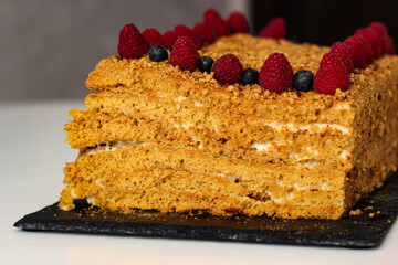 A homemade delicious layered honey cake, decorated with raspberries and blueberries on top, close-up. It's so tasty! Let's try it!