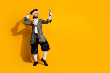Young man dressed as a nobleman from a classic era posing against a yellow background while taking...