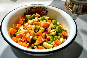 Bright and appetizing fruit salad in a white bowl with a floral pattern. The salad contains pieces of kiwi, tangerine, apple, and banana, creating a colorful and healthy dish.
