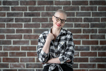 Obraz premium Portrait of a beautiful young caucasian woman with shaved head. Female cancer survivor. Smiling with Glasses Posing Confidently in a Studio. A portrait showcasing strength. Model Has Glaucoma