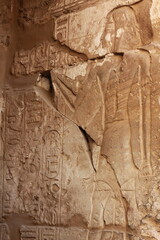 Damaged drawings and hieroglyphs on the wall of the Karnak Temple in Luxor, Egypt. Image of ancient Egyptian person standing next to ancient script.