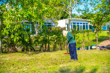 A janitor cleans the lawn area from leaves and mown grass. Hotel cleaning service.
