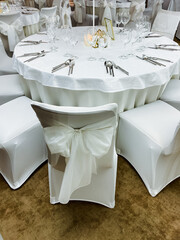A beautifully arranged round table adorned with elegant white linens, featuring lovely bows on the chairs that enhance the decor, creating an inviting atmosphere for guests at the event