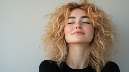 Blonde woman with curly hair smiling in front of a neutral background, bright light illuminating her face, soft focus, and plenty of empty space.