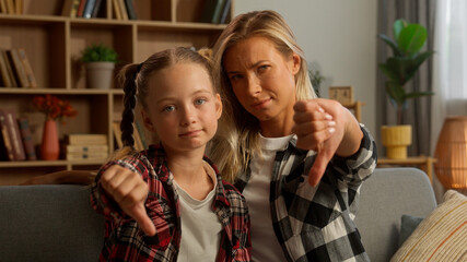 Dissatisfied Caucasian child girl schoolgirl female mother parent demonstrating thumb down with...