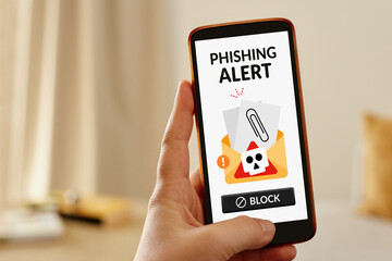 Female hand holding a smartphone displaying a phishing alert, symbolizing online scam warnings.