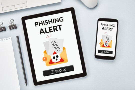 Overhead shot of a phishing alert on a vertically placed tablet and smartphone, both positioned on a gray table. A warning of digital scams in everyday technology.