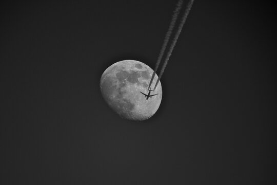image of a plane flying over the moon in the sky. Moon and airplane in the sky with contrail