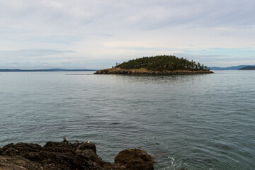 Deception Island is seen on a cloudy day from the beach of beautiful Deception Pass State Park,...
