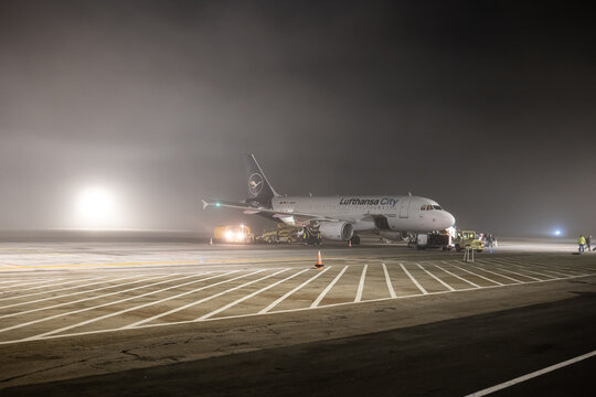 27-12-2024 Timișoara Traian Vuia International Airport, Romania. Lufthansa City commercial airplane on the runway waiting to be serviced on a foggy winter night. People deboarding in the background