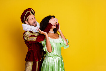 Couple in Historical Costumes Enjoying a Playful Moment Together on a Bright Yellow Background