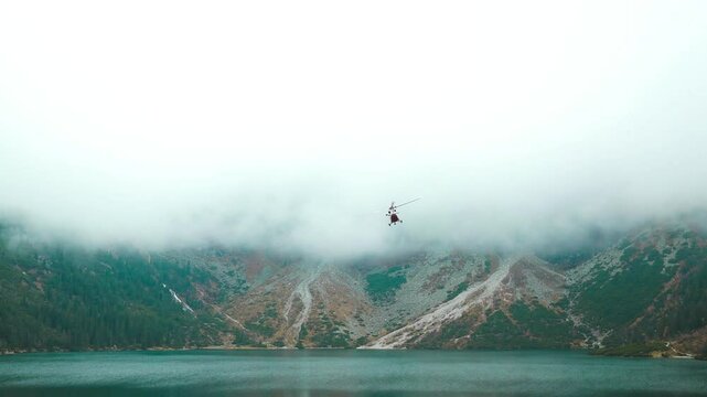 Red helicopter is flying between mountains peak near a Morsie oko, summer time. High quality FullHD footage