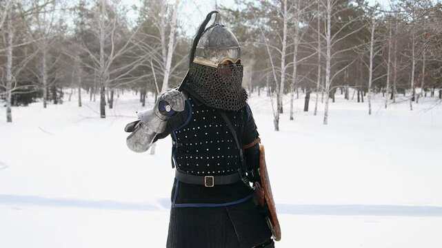 Medieval Central Asian warrior in full armor and helmet with closed face, posing standing against winter park background with sword and shield in hands, camera movement, selective focus.