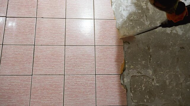 Builders remove old floor tiles with chisel, perforator and hammer, preparing surfaces for repair. Dust and debris accumulate in process of transforming spaces