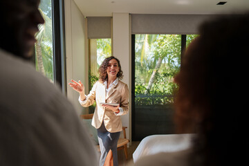 Female real estate agent in business attire presents residential property to diverse young couple...