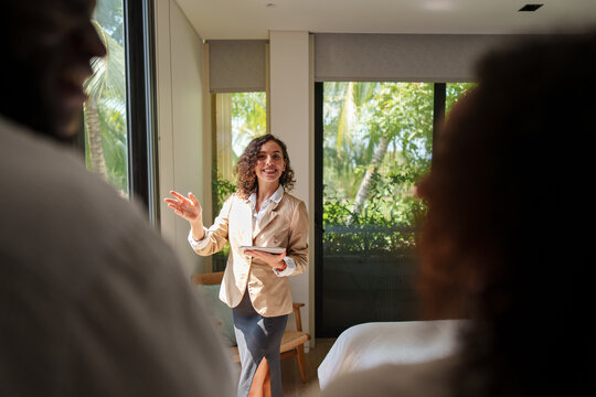 Female real estate agent in business attire presents residential property to diverse young couple during sunny afternoon house viewing session.
