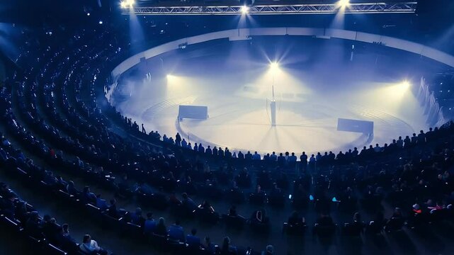 High angle view of a large audience in a futuristic circular hall, illuminated by bright stage spotlights