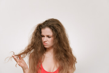 A young woman with voluminous, curly hair looks frustrated as she examines her dry, tangled strands.The struggle of maintaining unruly hair, highlighting beauty challenges and self-care. Bad hair day