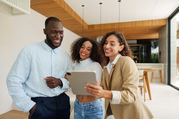 Female real estate professional in business attire consults with diverse couple using tablet device...