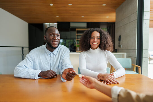 Diverse couple reviews property documents with real estate agent in modern office setting during important homebuying consultation meeting.