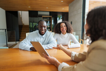 Professional real estate agent in business attire consults with diverse couple at modern office,...