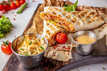 Shawarma with chicken is served on a wooden board with sauce and cabbage salad