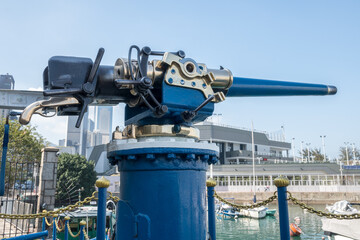 Jardine Noonday Gun in Hong Kong: A vintage naval cannon, painted blue and brass, is mounted on a pier with a golden chain and posts.