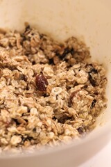 The process of preparing homemade oatmeal cookies - raw dough from oatmeal, flour, dried fruit, butter, honey in a bowl