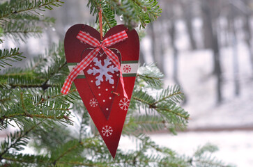 red wooden heart with ornament , christmas tree decoration hangs on a fir tree branch .Winter holidays season greeting ,christmas tree decorations. Free copy space.