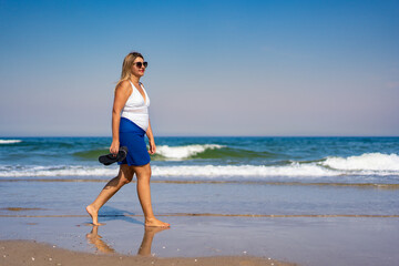 Beautiful middle aged woman walking on sandy beach in summertime. Side view