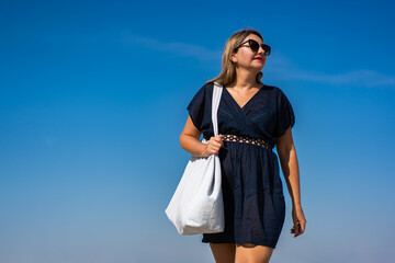 Beautiful middle-aged woman tourist walking against background of blue sky in summer