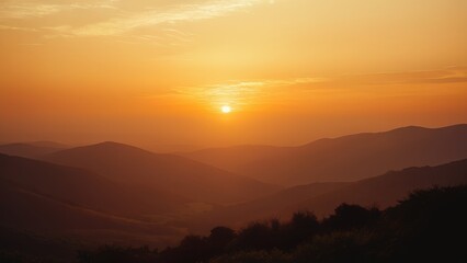 Obraz premium Stunning sunset over mountain range. Warm golden light illuminates the hazy landscape. Perfect for travel, nature, and serenity themes