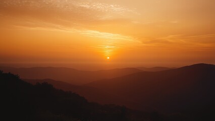 Fototapeta premium Stunning sunset over mountain range. Warm golden light illuminates the hazy landscape. Perfect for travel, nature, and serenity themes